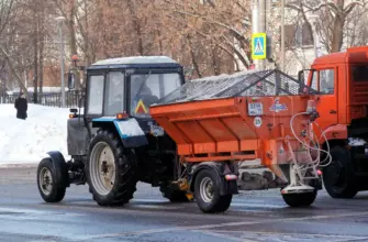 трактор Беларус с прицепным пескоразбрасывателем зимой на заснеженной городской улице